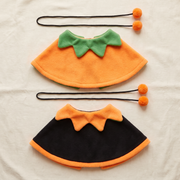 Both sides of the reversible cape laid flat, orange with a green collar and black with an orange collar