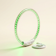 The glow collar standing upright on a warm ivory studio backdrop, LED points lit green, USB cable coiled beside it