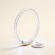 The glow collar standing upright on a warm ivory studio backdrop, LED points lit white, USB cable coiled beside it